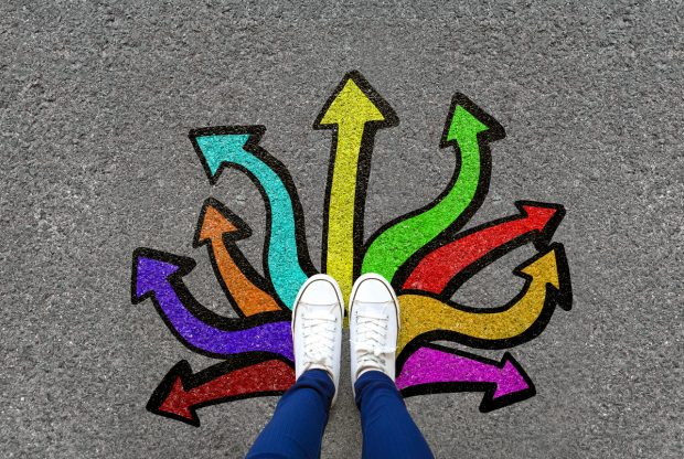 Feet and arrows on road background. Pair of foot standing on tarmac road with colorful graffiti arrow sign choices, creative and idea concept. Selfie woman wearing white shoe or sneaker. Top view.